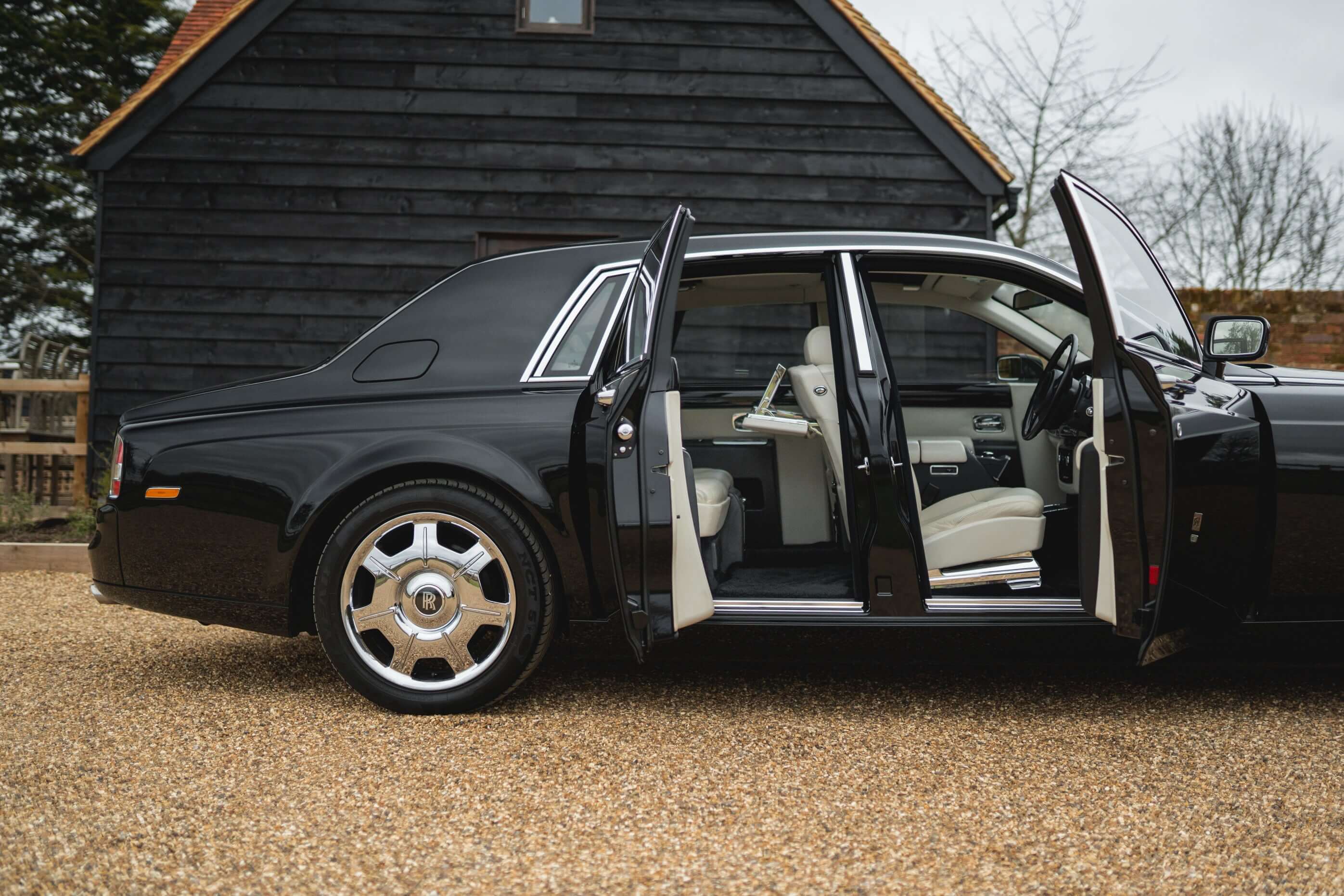 Elegant black Rolls-Royce Phantom with open doors, showcasing its opulent cream leather interior. Experience luxury chauffeur hire with SJ Chauffeurs, offering VIP, executive, and wedding transport services across the UK. Travel in sophistication—book your Rolls-Royce today!