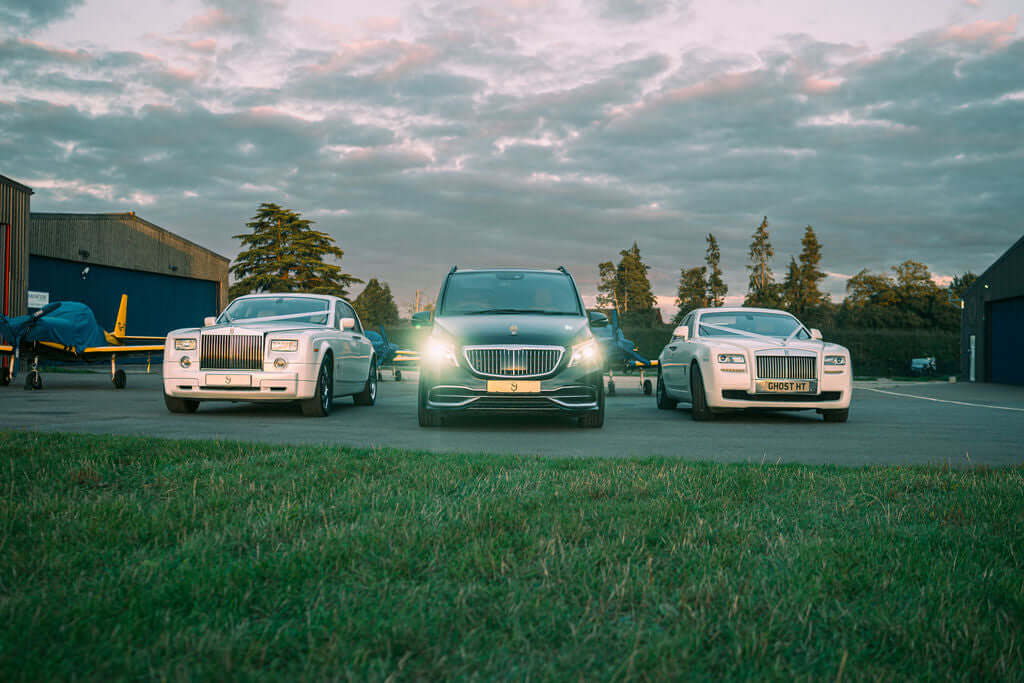 Prestigious luxury chauffeur fleet featuring a Rolls-Royce Phantom, Mercedes-Maybach, and Rolls-Royce Ghost parked at a private airfield at sunset. Experience first-class chauffeur hire with SJ Chauffeurs, specialising in VIP transport, executive travel, and wedding car hire across the UK. Book your luxury ride today!